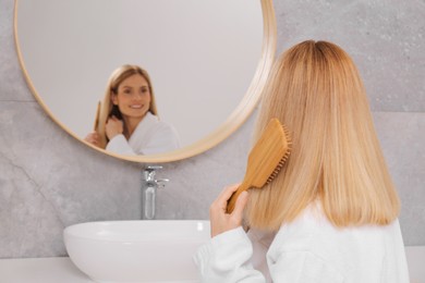 Photo of Woman brushing her hair near mirror in bathroom