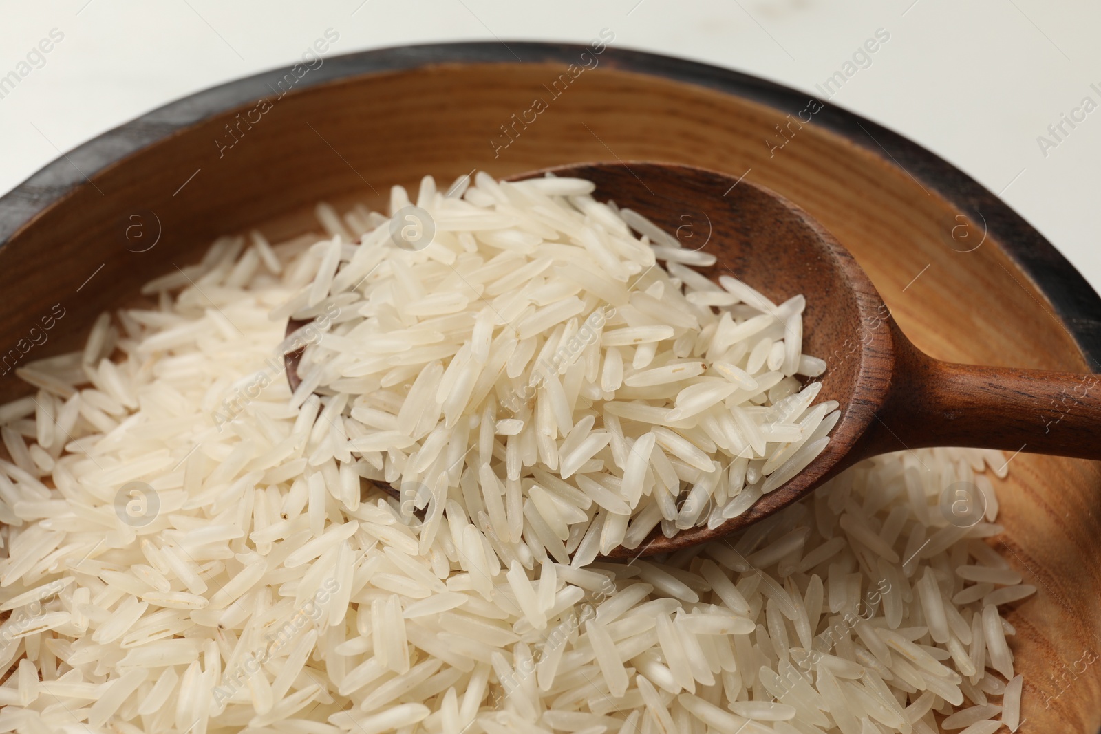 Photo of Raw basmati rice with spoon in wooden bowl on table, closeup