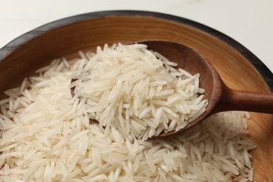 Photo of Raw basmati rice with spoon in wooden bowl on table, closeup