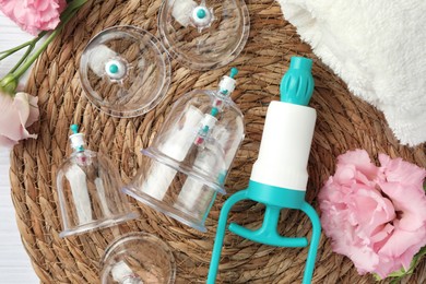 Photo of Plastic cups, hand pump and flowers on white table, flat lay. Cupping therapy