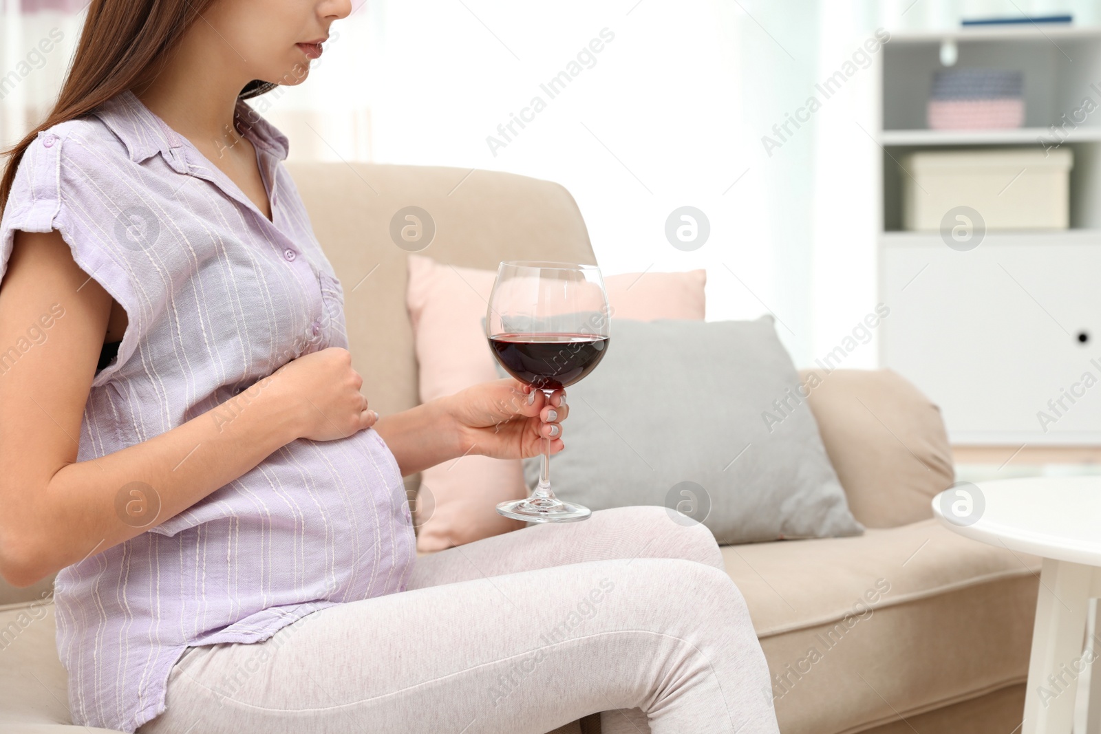 Photo of Future mother with glass of wine at home, closeup. Alcohol abuse during pregnancy