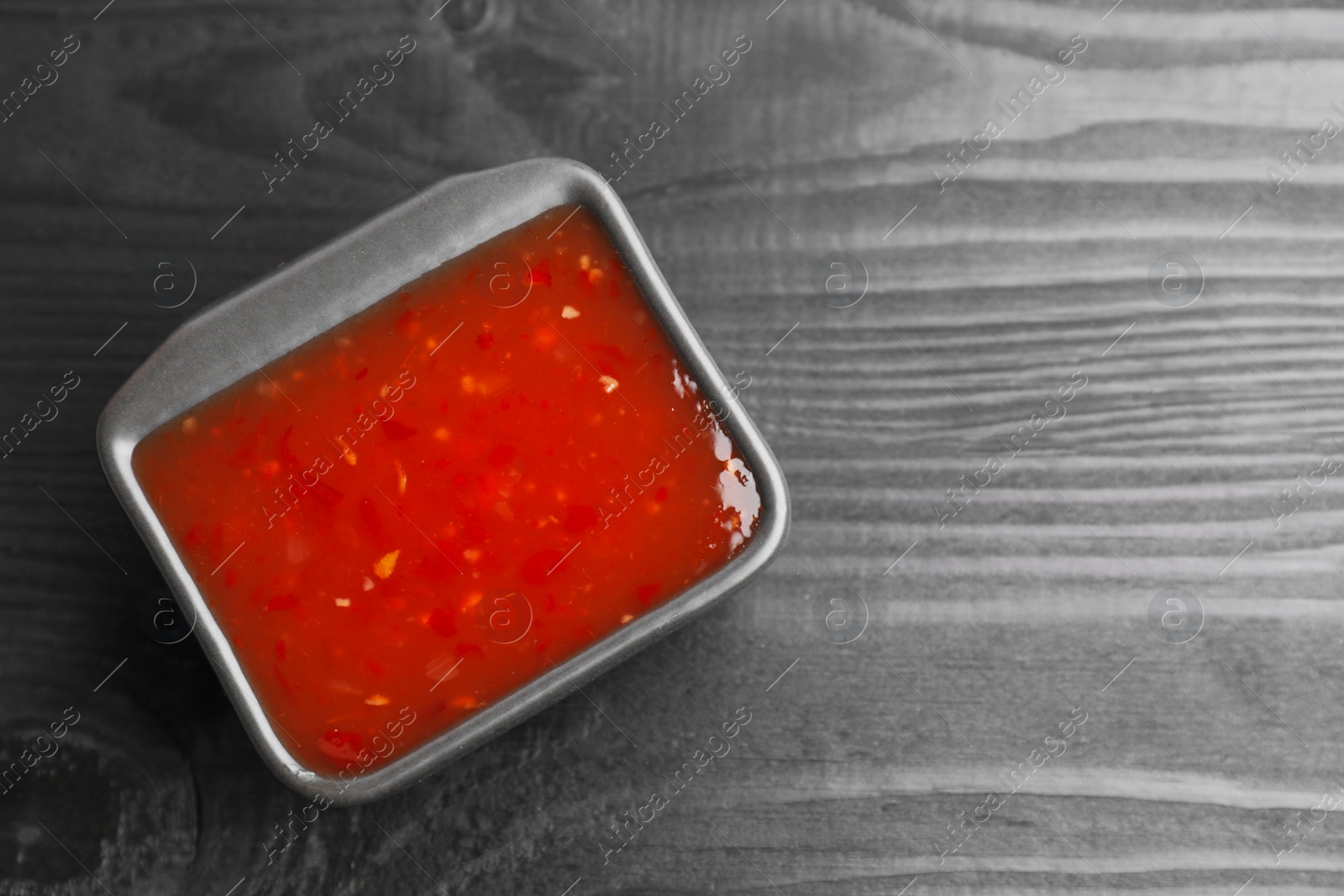 Photo of Spicy chili sauce in bowl on black wooden table, top view. Space for text