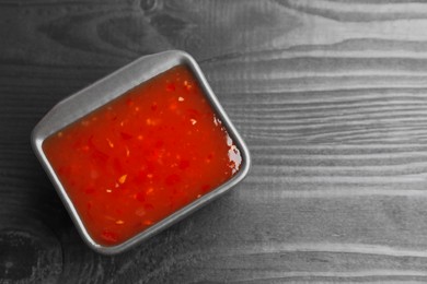 Photo of Spicy chili sauce in bowl on black wooden table, top view. Space for text