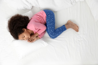 Photo of Cute little African-American girl sleeping in bed, top view