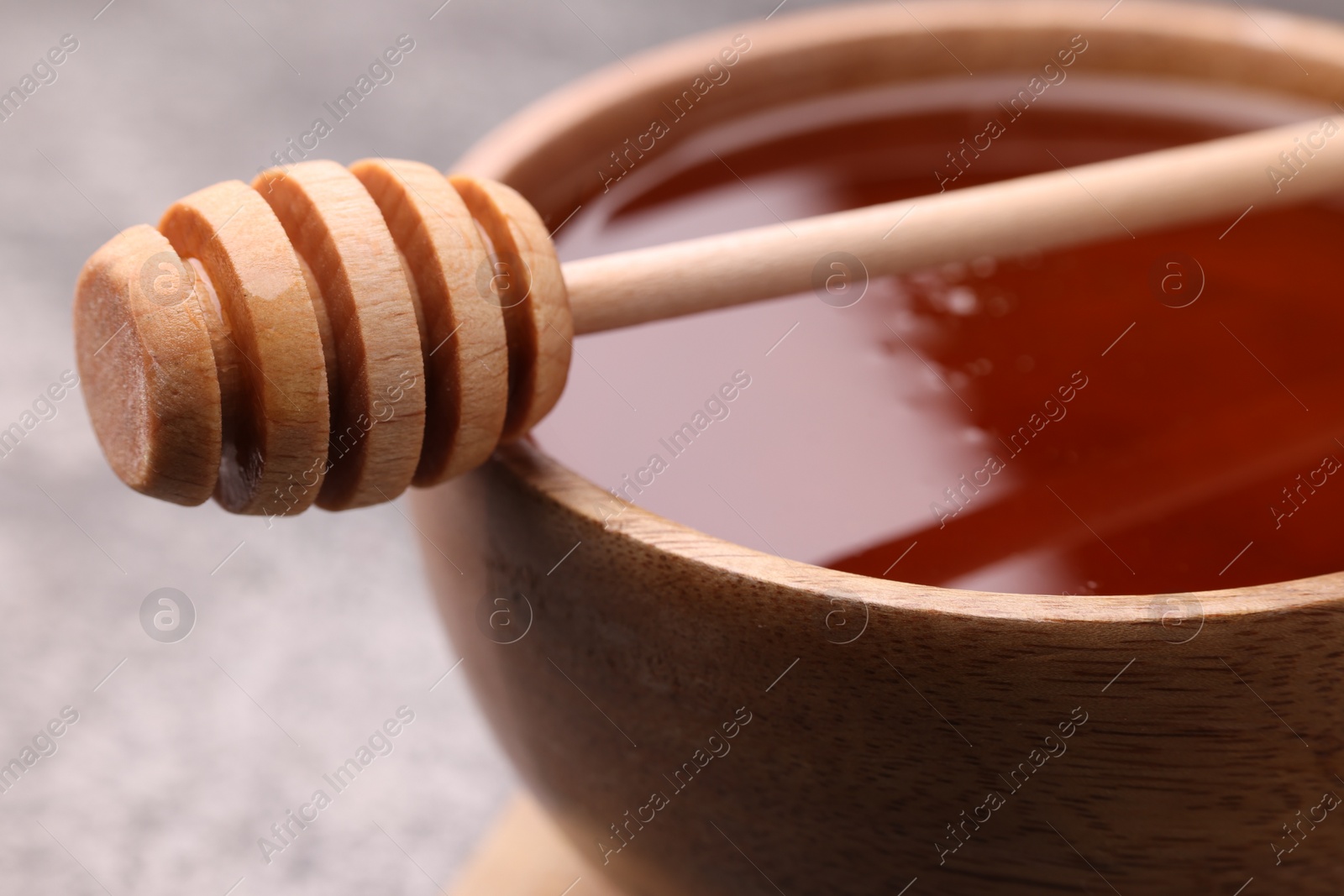 Photo of Delicious honey in bowl and dipper on grey table, closeup