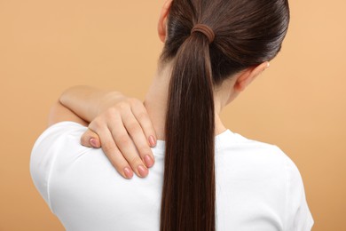 Woman touching her neck on beige background, back view
