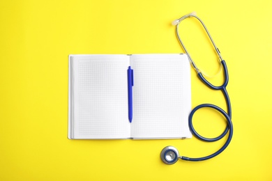 Copybook with pen and stethoscope on color background, flat lay. Medical care