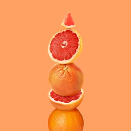 Stacked cut and whole grapefruits on orange background