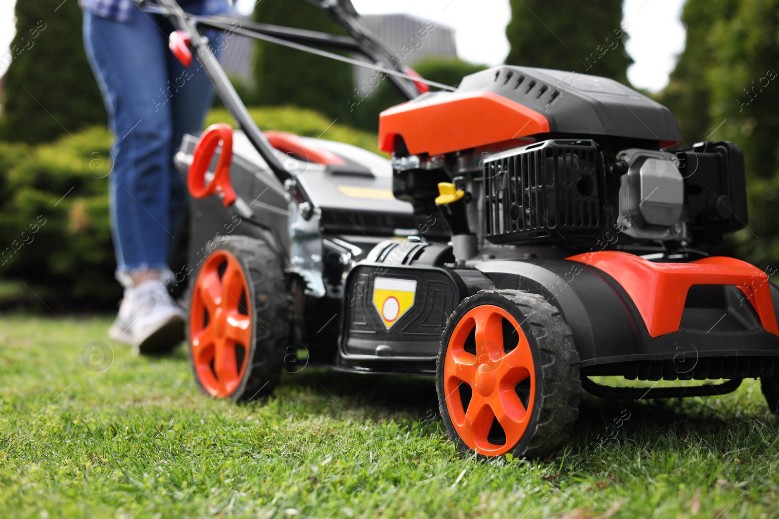Photo of Woman cutting green grass with lawn mower in garden, selective focus
