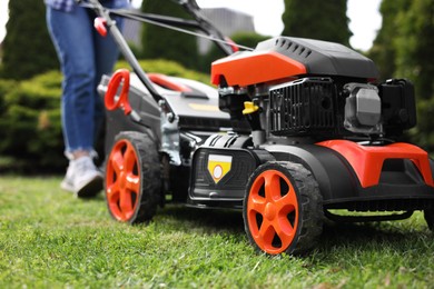 Photo of Woman cutting green grass with lawn mower in garden, selective focus