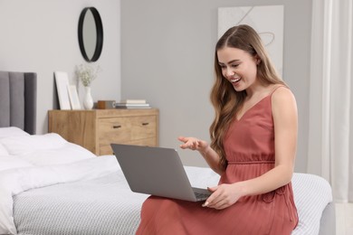 Happy woman having video chat via laptop on bed in bedroom