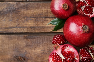 Flat lay composition with ripe pomegranates on wooden background, space for text