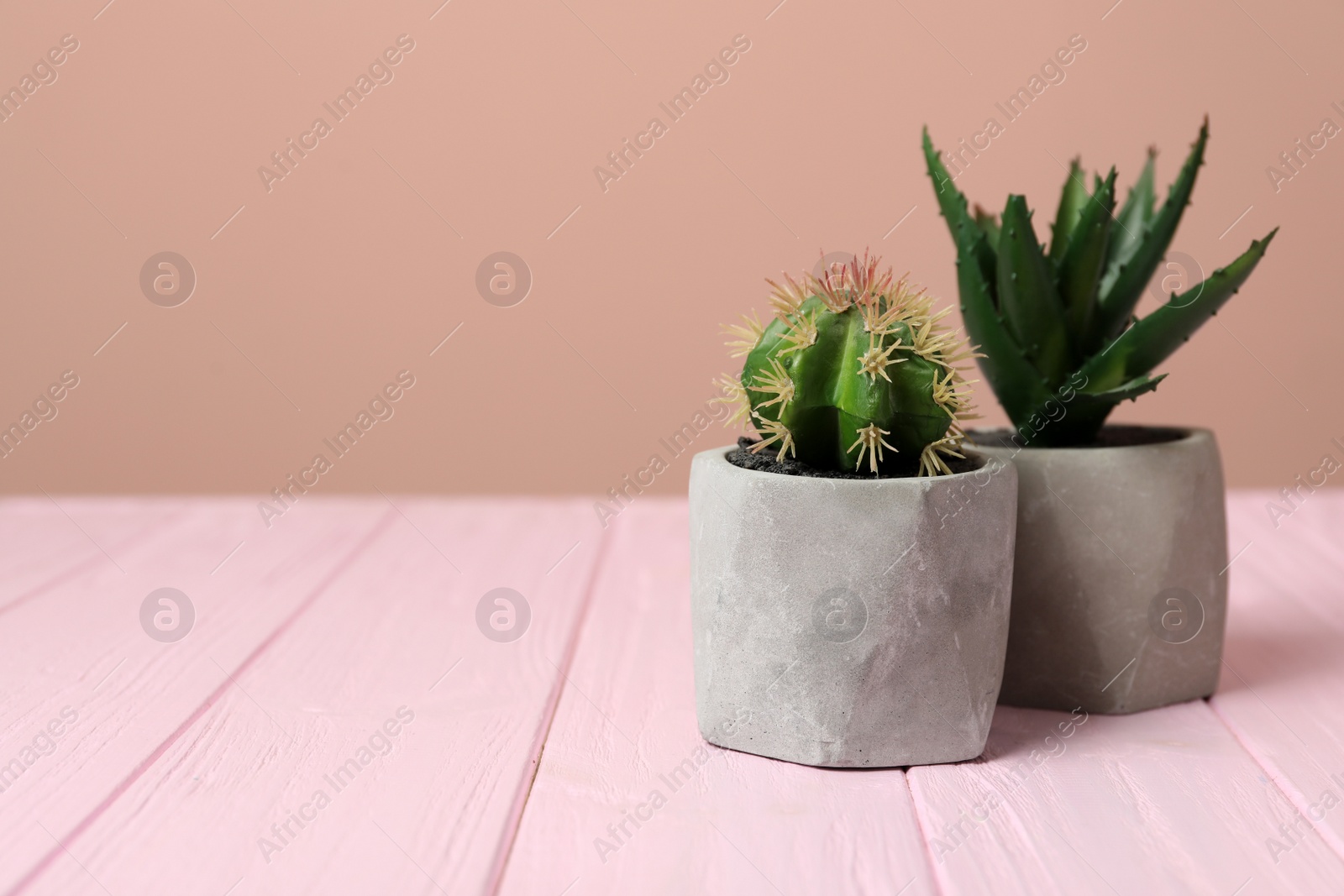 Photo of Artificial plants in cement flower pots on pink wooden table. Space for text
