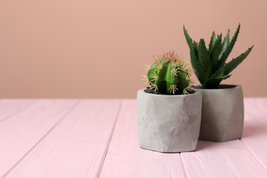 Artificial plants in cement flower pots on pink wooden table. Space for text