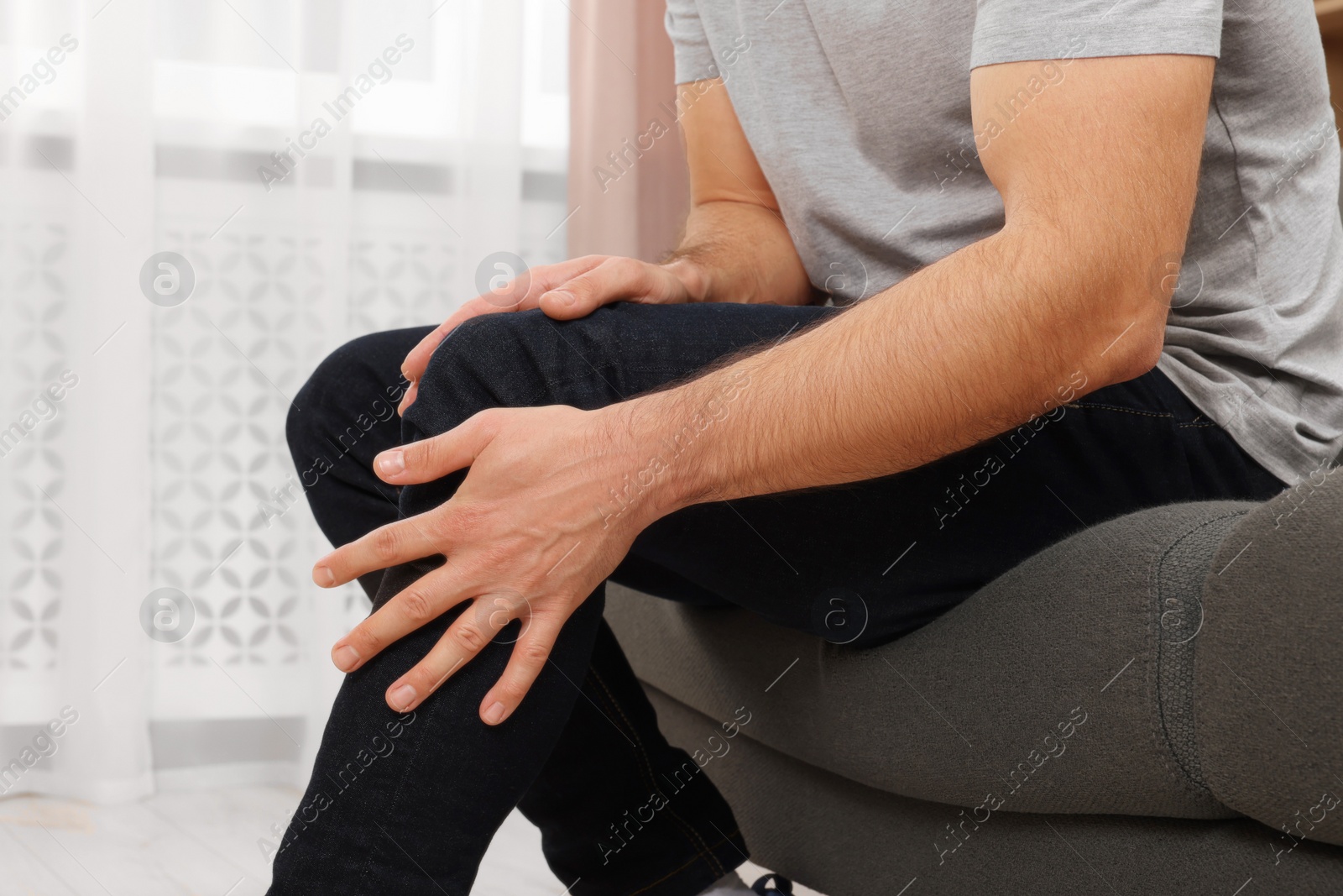 Photo of Man suffering from knee pain on sofa indoors, closeup