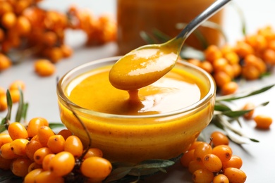 Photo of Spoon with delicious sea buckthorn jam over bowl on light table, closeup