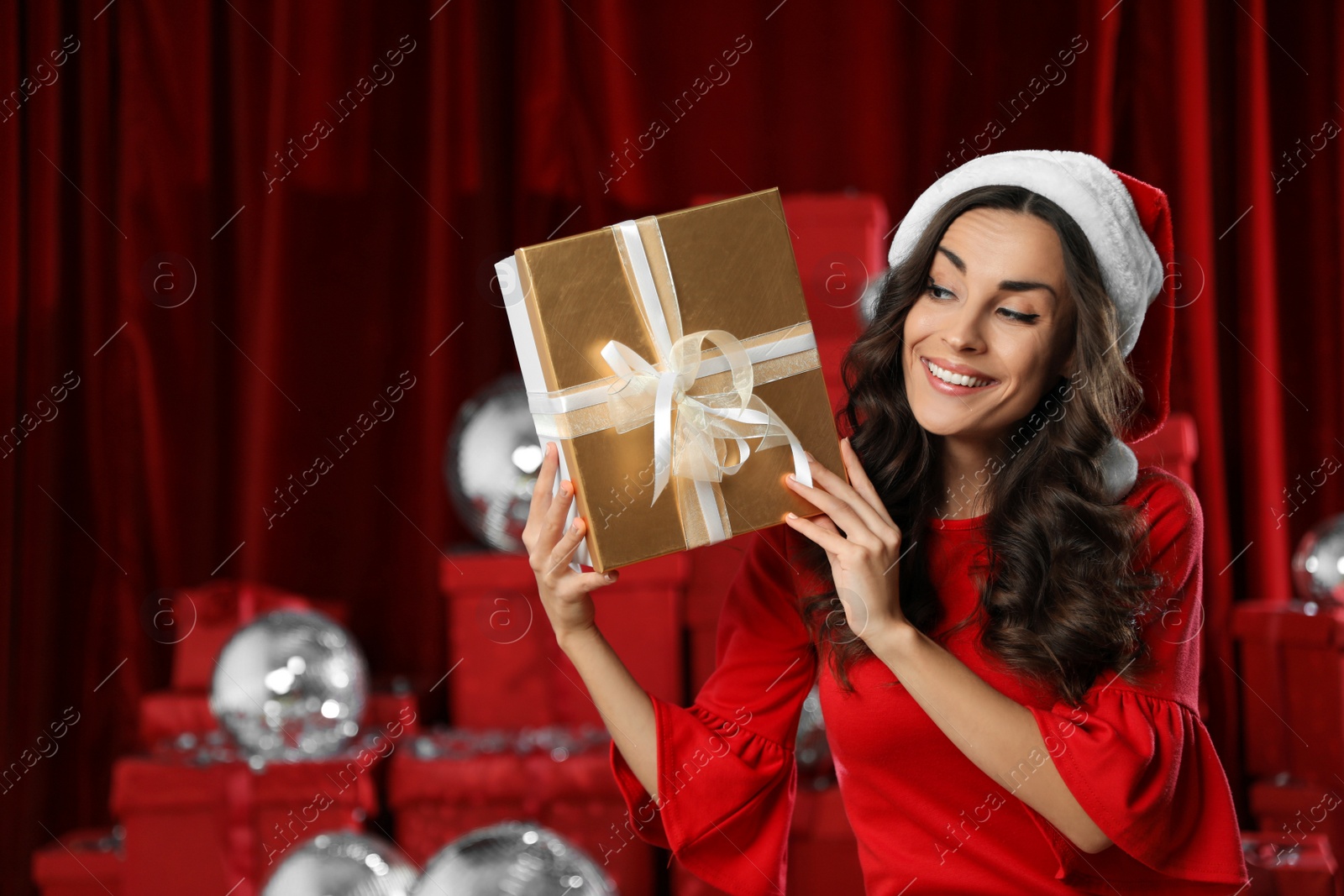 Photo of Beautiful woman in Christmas costume with gift near pile of presents indoors