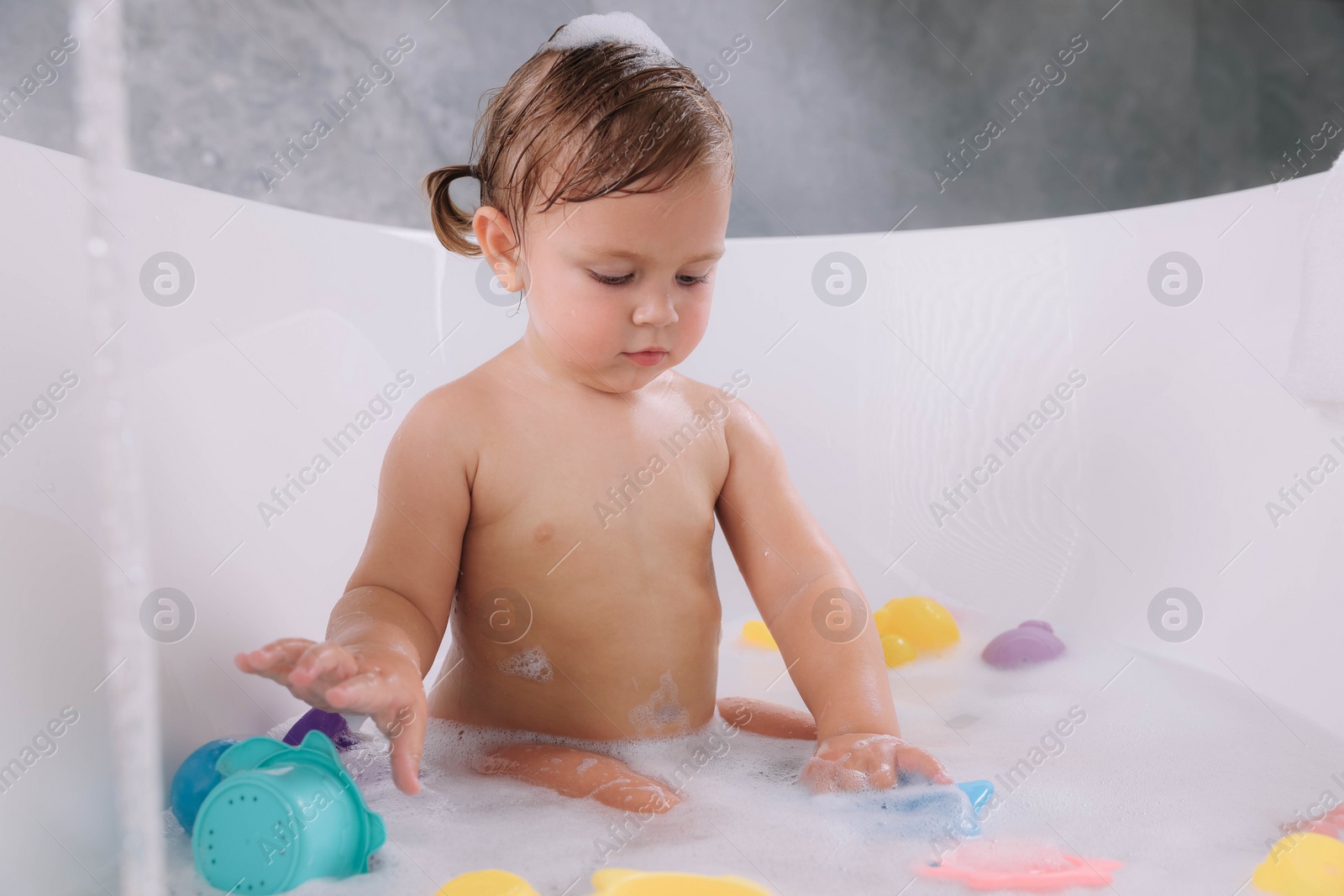 Photo of Cute little girl taking bubble bath with toys indoors