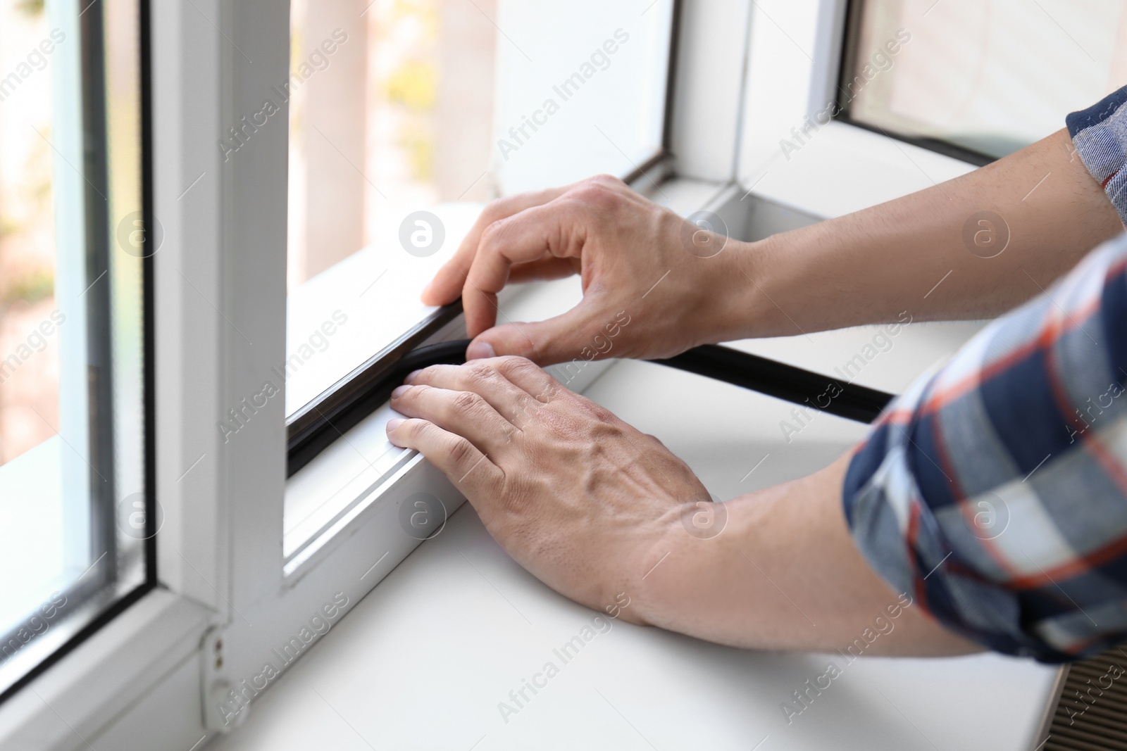 Photo of Young man putting sealing foam tape on window indoors