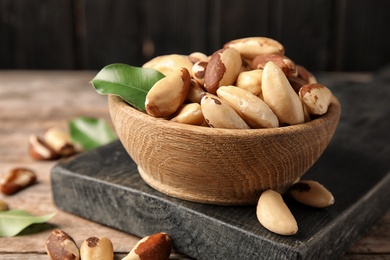 Photo of Wooden board with bowl of tasty Brazil nuts on table