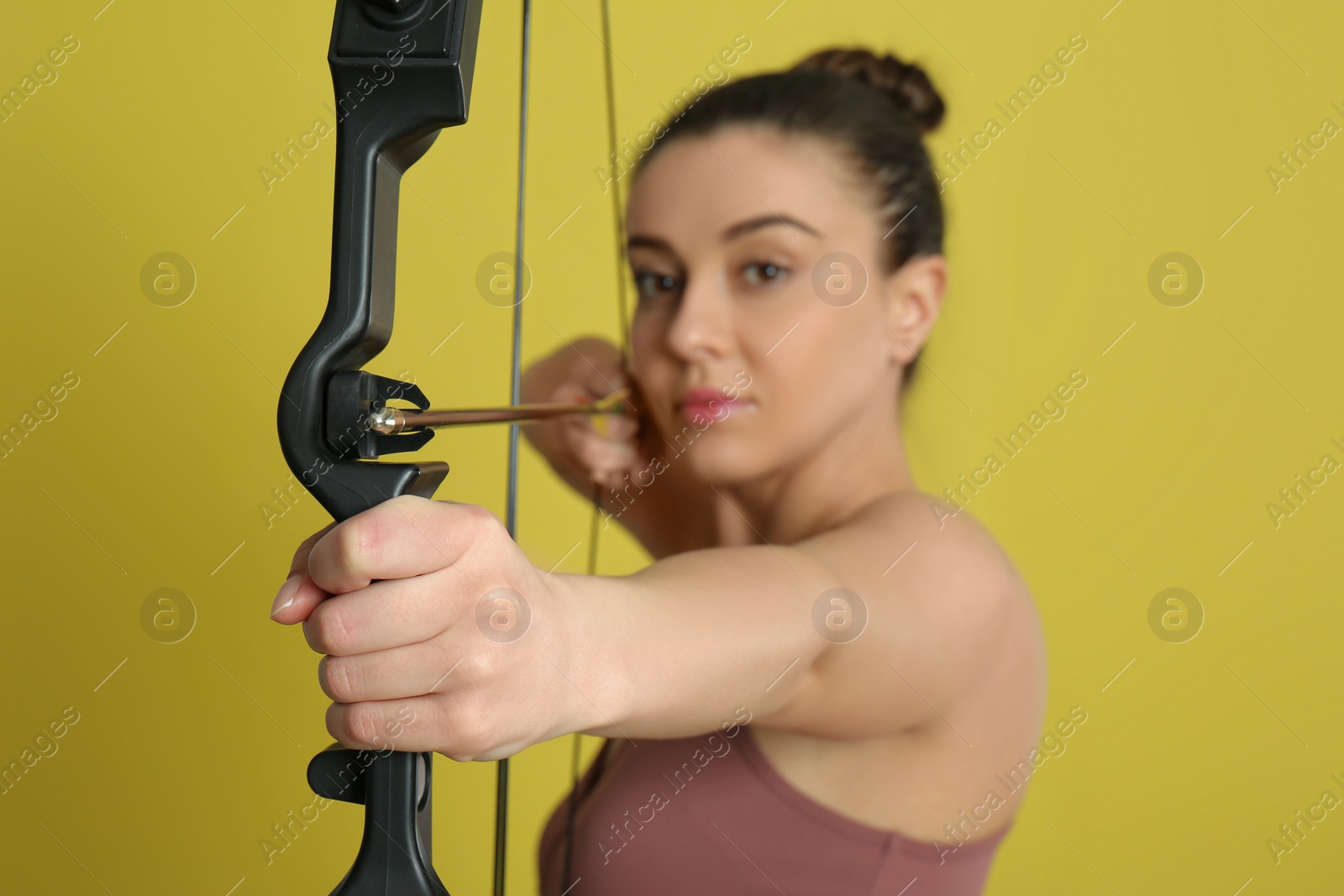 Photo of Woman with bow and arrow practicing archery against yellow background, focus on hand