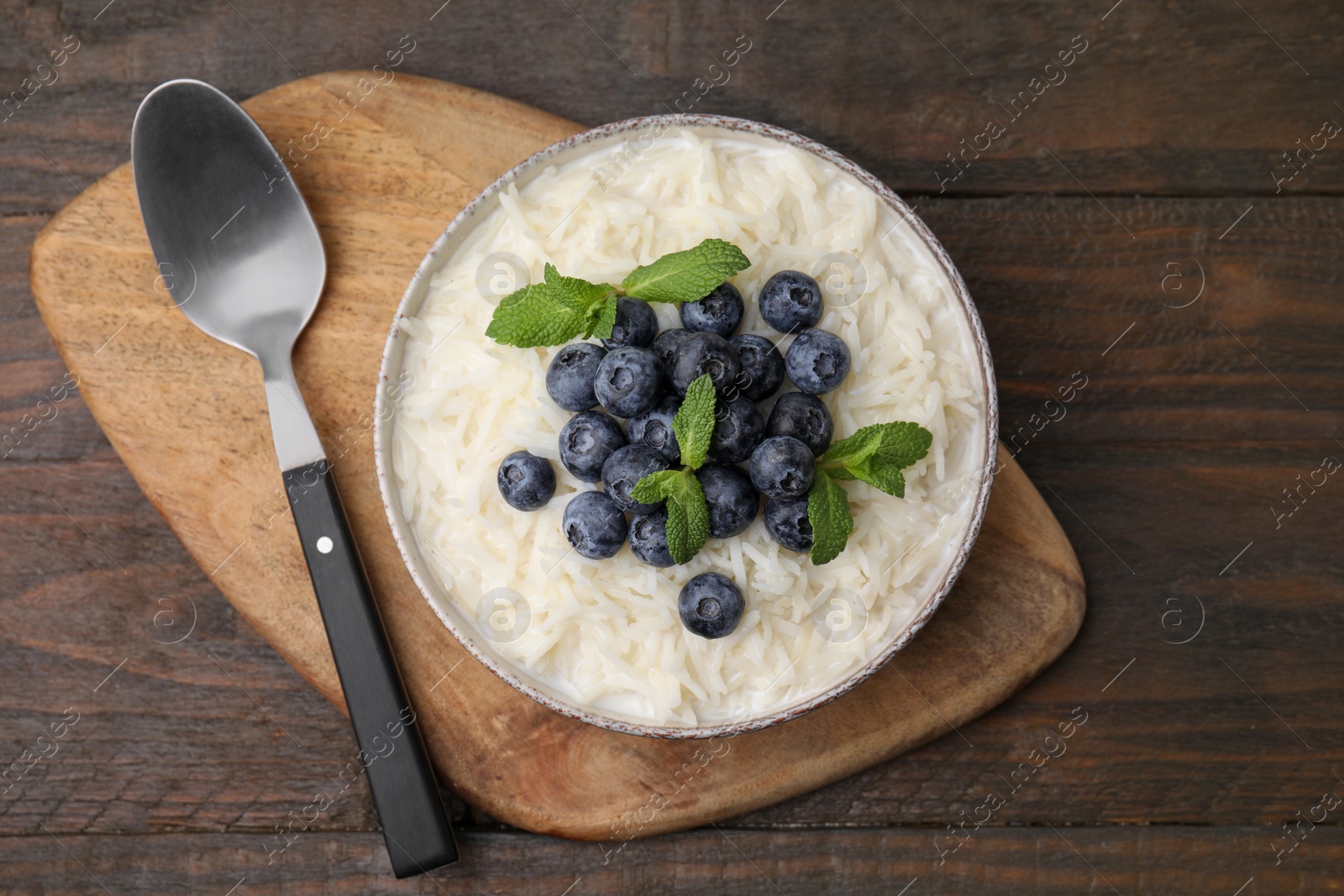 Photo of Bowl of delicious rice porridge with blueberries and mint served on wooden table, top view