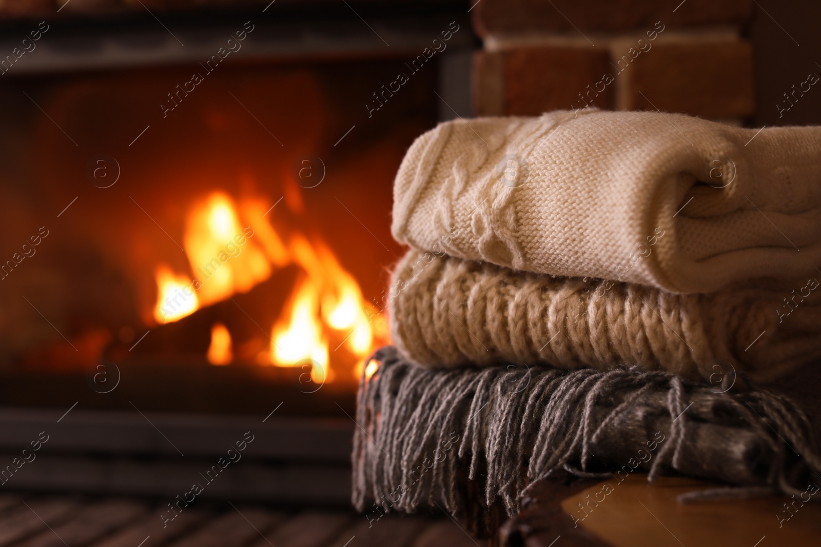 Photo of Stack of knitwear near fireplace with burning wood indoors. Winter vacation