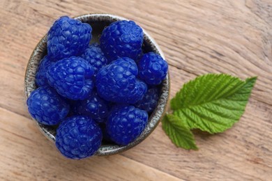 Image of Many fresh blue raspberries in bowl on wooden table, top view