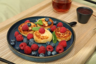 Photo of Delicious cottage cheese pancakes with fresh berries and mint served on wooden bed tray