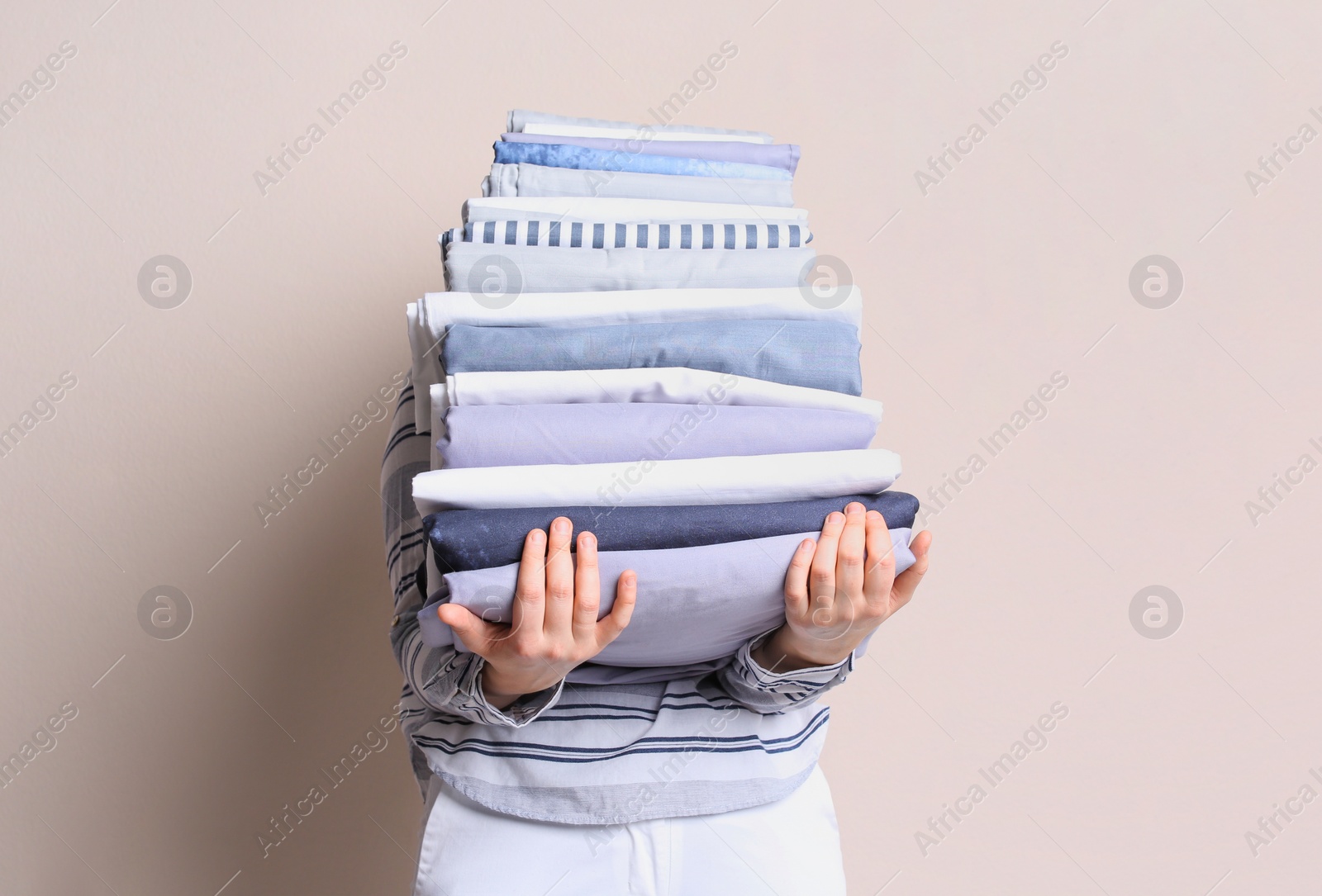 Photo of Woman holding stack of clean bed linens on beige background