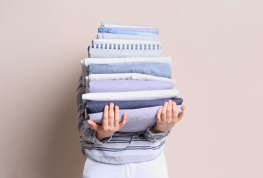 Woman holding stack of clean bed linens on beige background