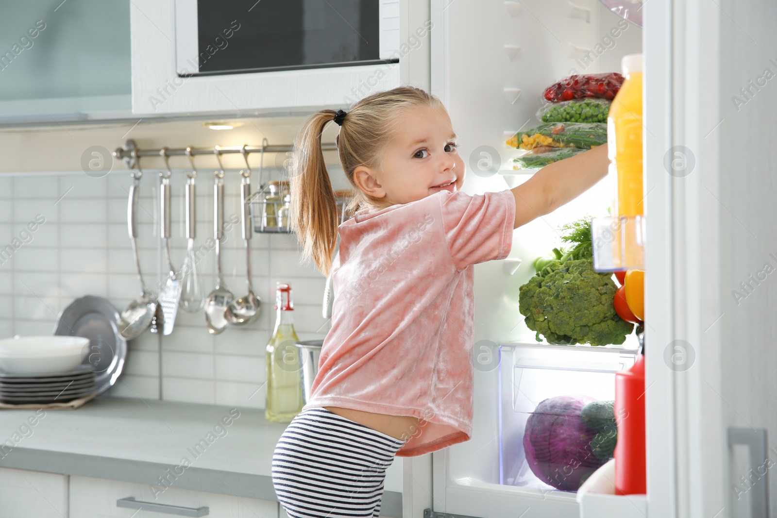 Photo of Cute girl choosing food from refrigerator in kitchen