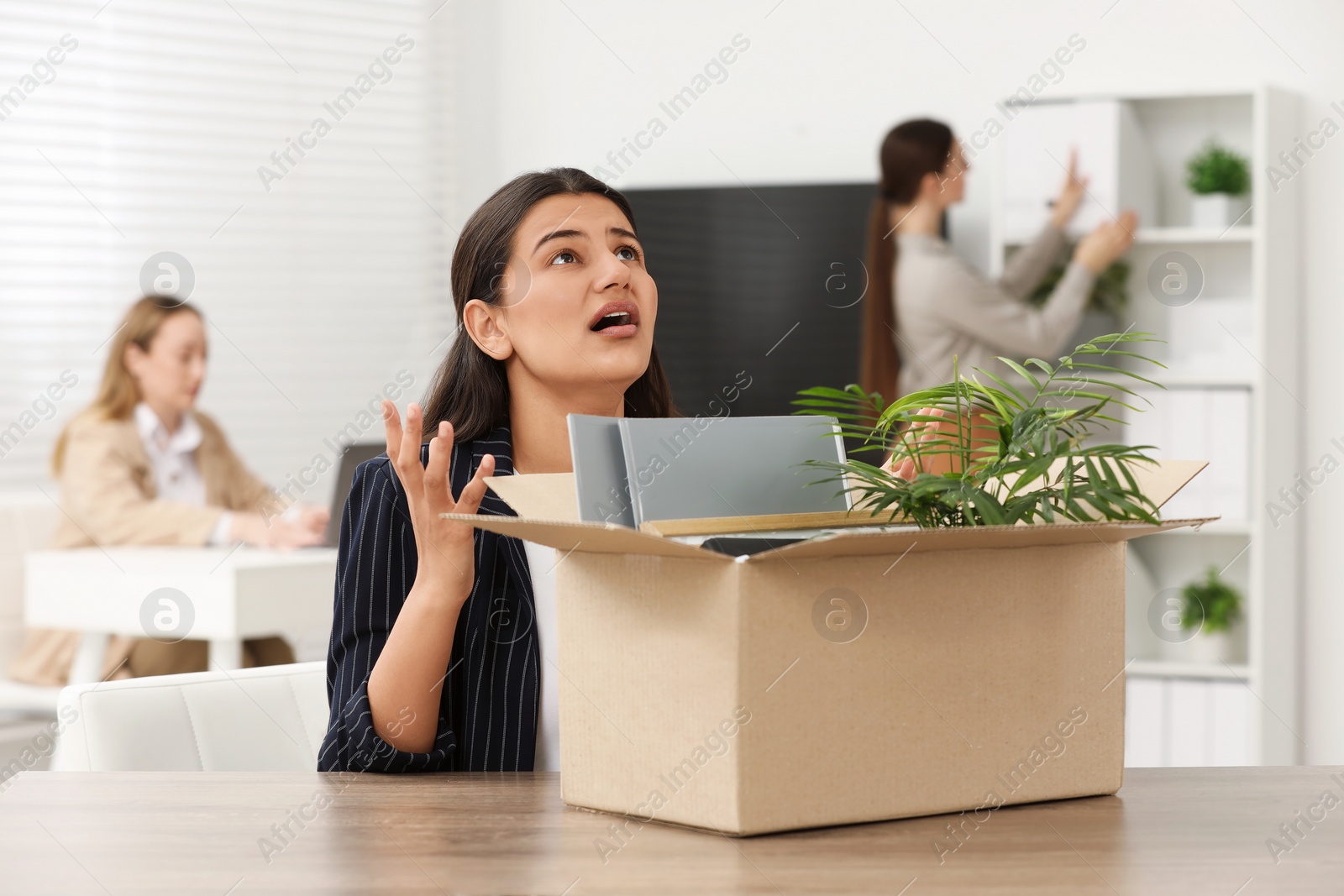 Photo of Unemployment problem. Woman with box of personal belongings at table in office