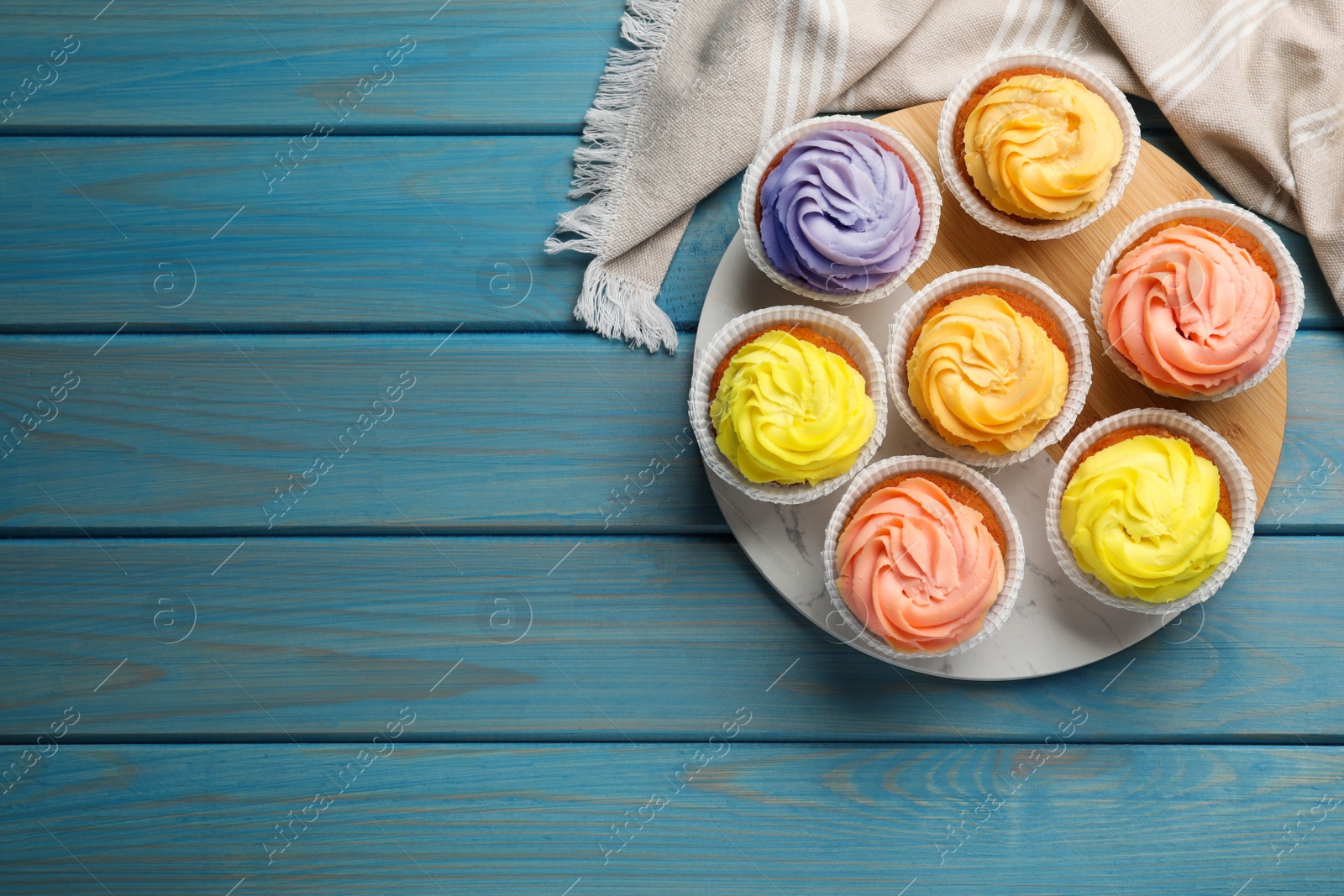 Photo of Stand with tasty cupcakes on light blue wooden table, flat lay. Space for text