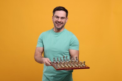 Smiling man holding chessboard with game pieces on orange background