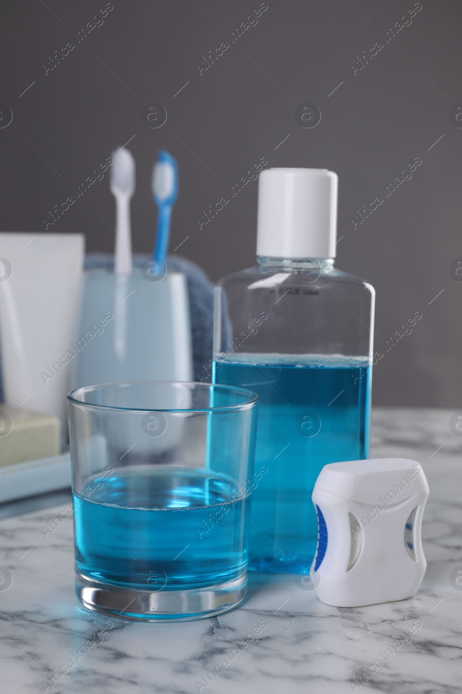 Photo of Fresh mouthwash in bottle, glass and dental floss on white marble table, closeup