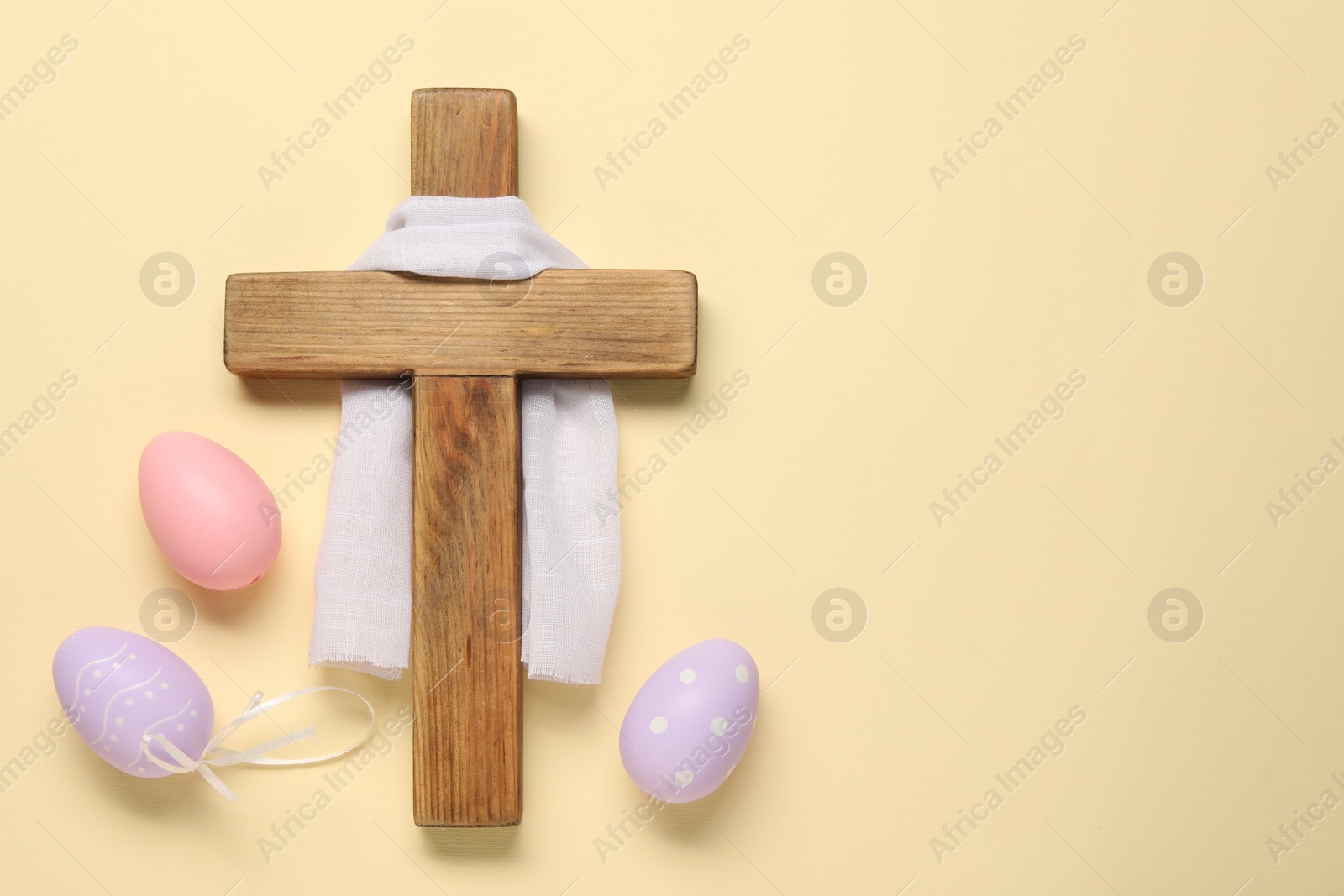 Photo of Wooden cross, white cloth and painted Easter eggs on beige background, flat lay. Space for text