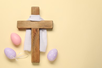 Wooden cross, white cloth and painted Easter eggs on beige background, flat lay. Space for text