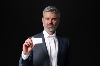 Handsome businessman holding blank business card on black background