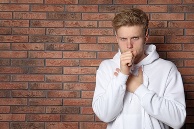 Photo of Handsome young man coughing near brick wall. Space for text
