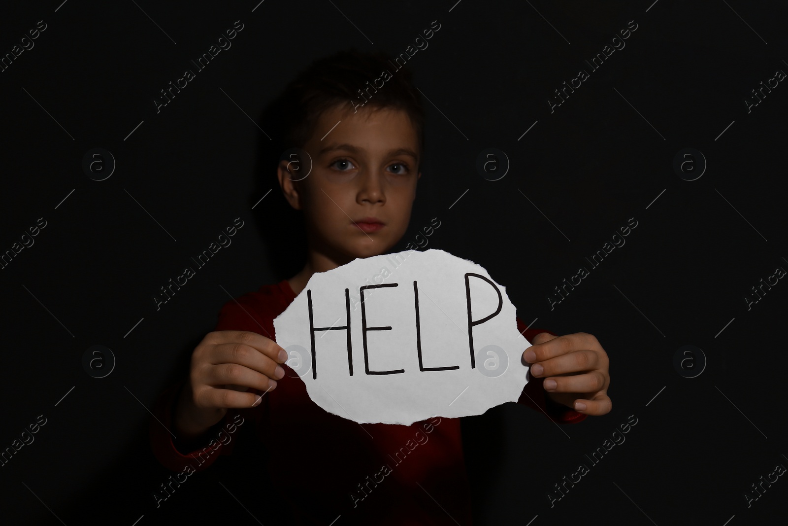 Photo of Abused little boy with sign HELP near black wall. Domestic violence concept