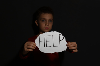 Photo of Abused little boy with sign HELP near black wall. Domestic violence concept