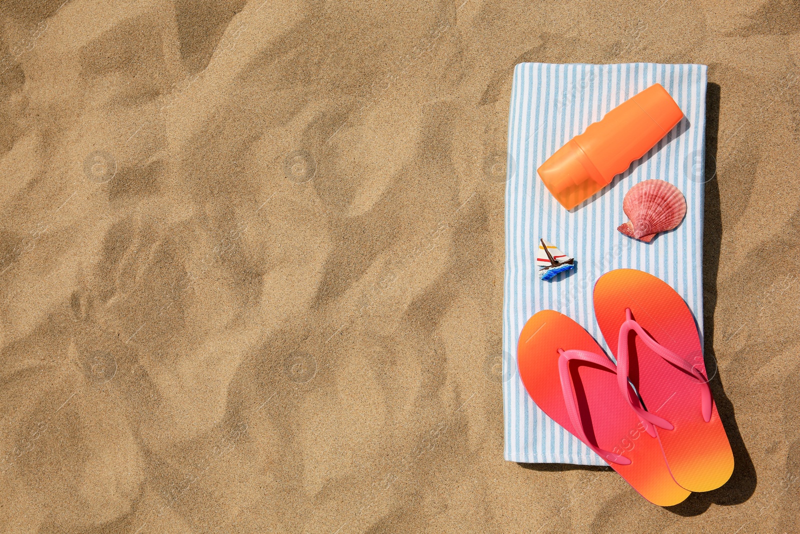 Photo of Bottle of sunscreen, flip flops and towel on sand, top view with space for text. Sun protection care