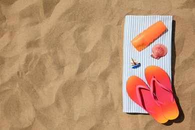 Photo of Bottle of sunscreen, flip flops and towel on sand, top view with space for text. Sun protection care