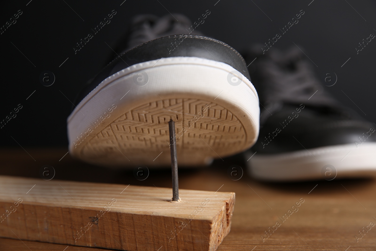 Photo of Metal nail in wooden plank and shoes on table, closeup