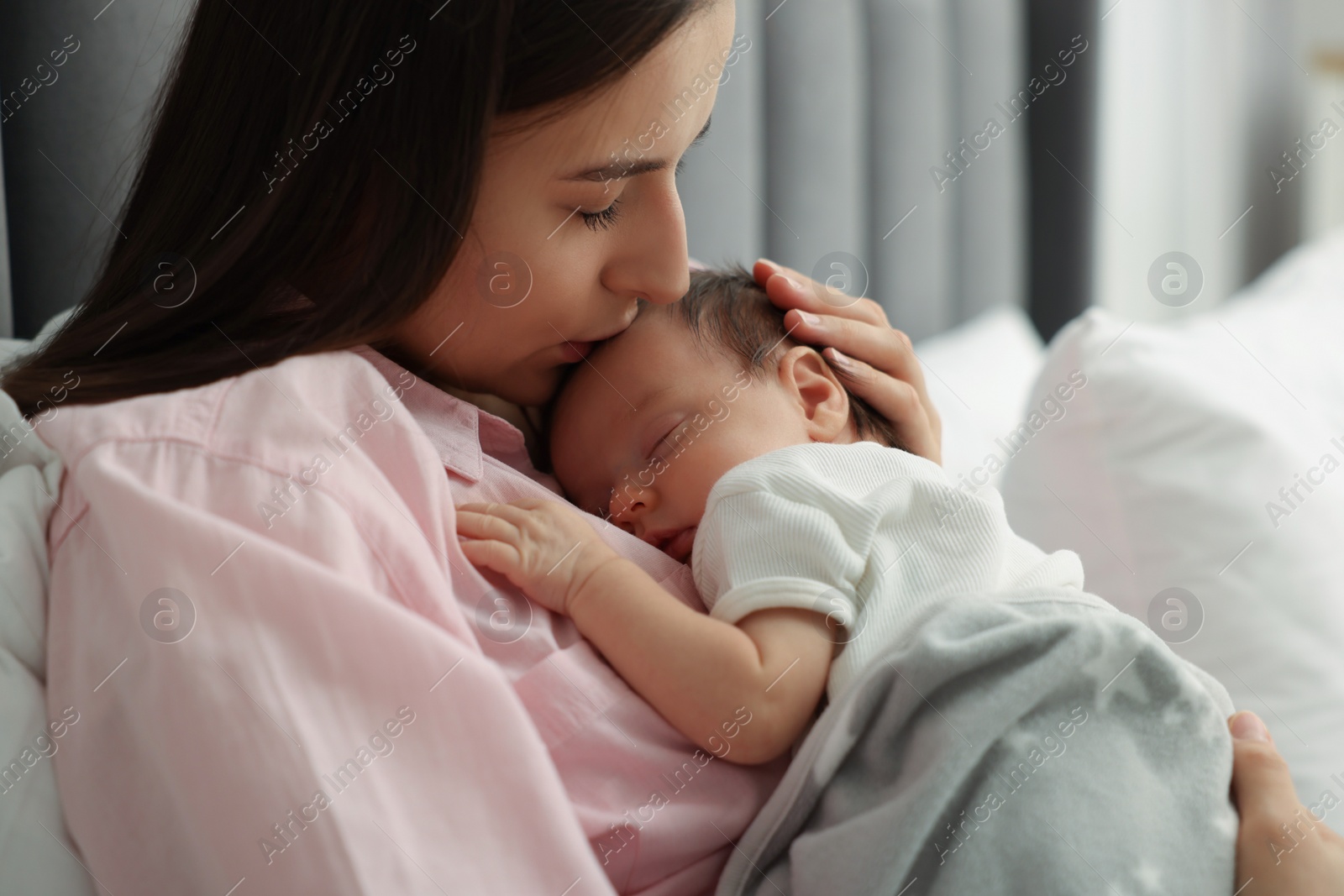 Photo of Mother kissing her sleeping newborn baby in bed