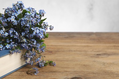 Bouquet of beautiful forget-me-not flowers and book on wooden table against light background, space for text