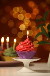 Photo of Stand with birthday cupcake on white table against blurred lights