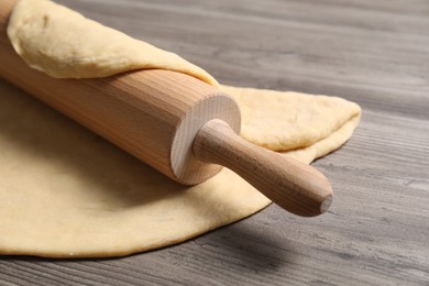 Photo of Raw dough and rolling pin on wooden table, closeup