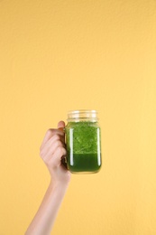 Young woman holding mason jar of healthy smoothie on color background